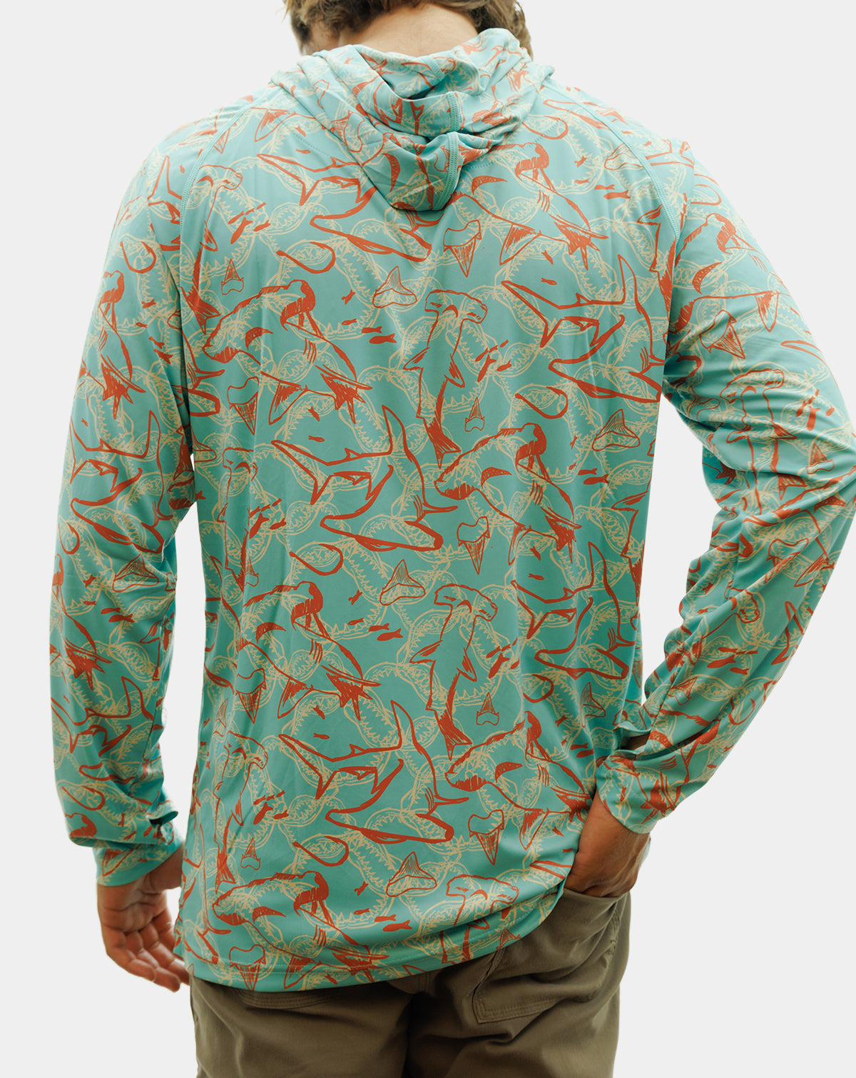 A man wearing a long-sleeve hooded performance shirt with a turquoise and orange fish pattern, featuring a black and white skull-and-crossbones logo on the left chest. Reel Sportswear Scurve fishing Hoody