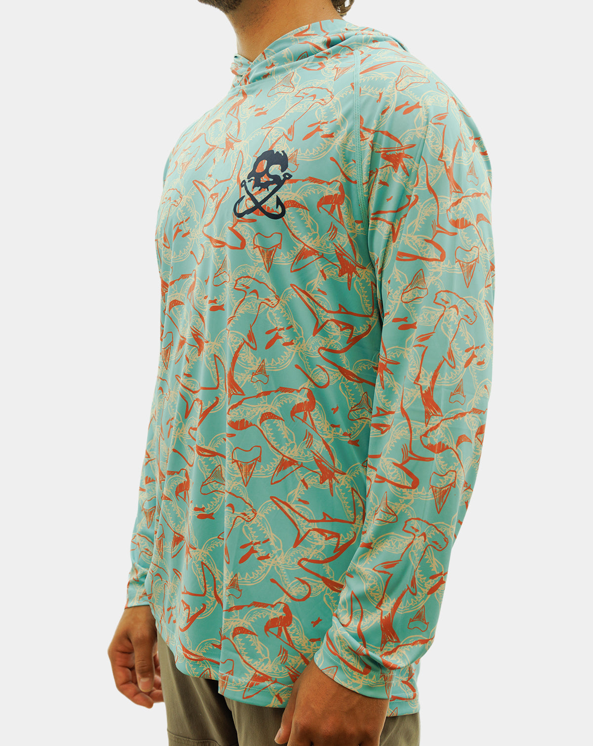 A man wearing a long-sleeve hooded performance shirt with a turquoise and orange fish pattern, featuring a black and white skull-and-crossbones logo on the left chest. Reel Sportswear Scurve fishing Hoody