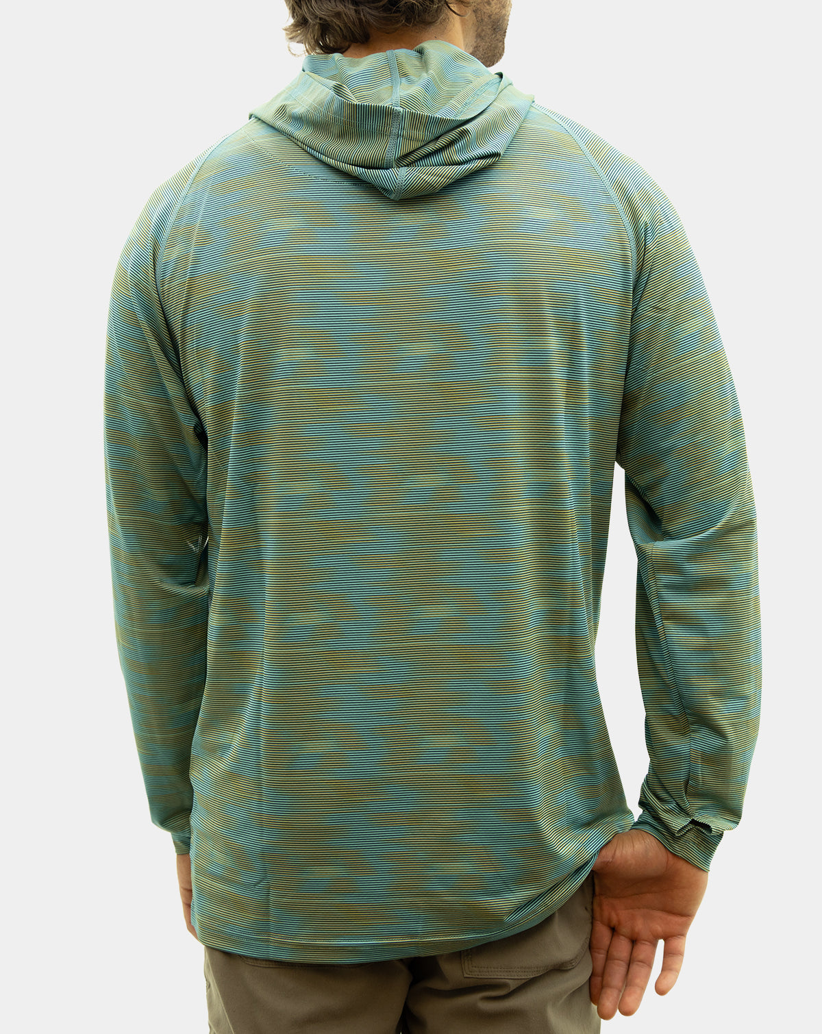 A man wearing the Static Pro+. viewed from the back wearing a long-sleeve hooded performance shirt with a blue-green and olive pattern, paired with khaki pants, against a light gray studio background. Reel Sportswear Fishing performance hoody.